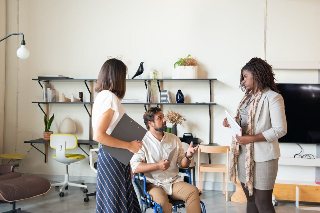 A Man Sitting on His Wheelchair while Talking to the Women Standing Beside Him